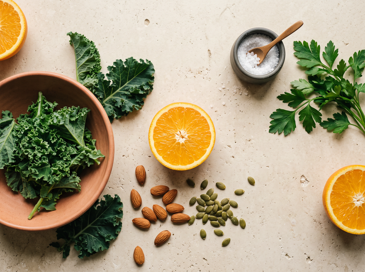 Fresh oranges, kale, almonds and pumpkin seeds on cream stone
